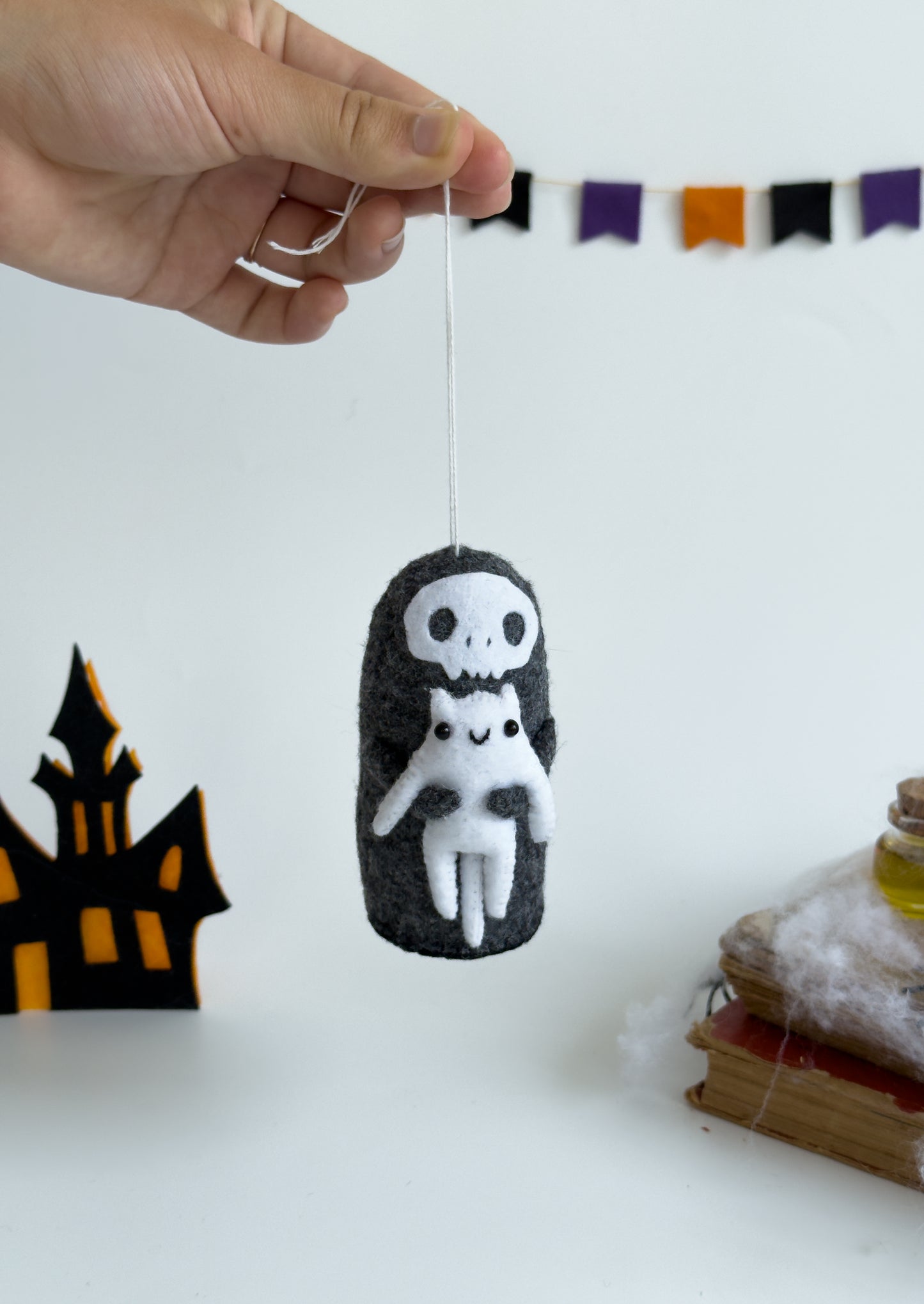 Gothic felt reaper doll next to spellbook and cobweb props – spooky setting