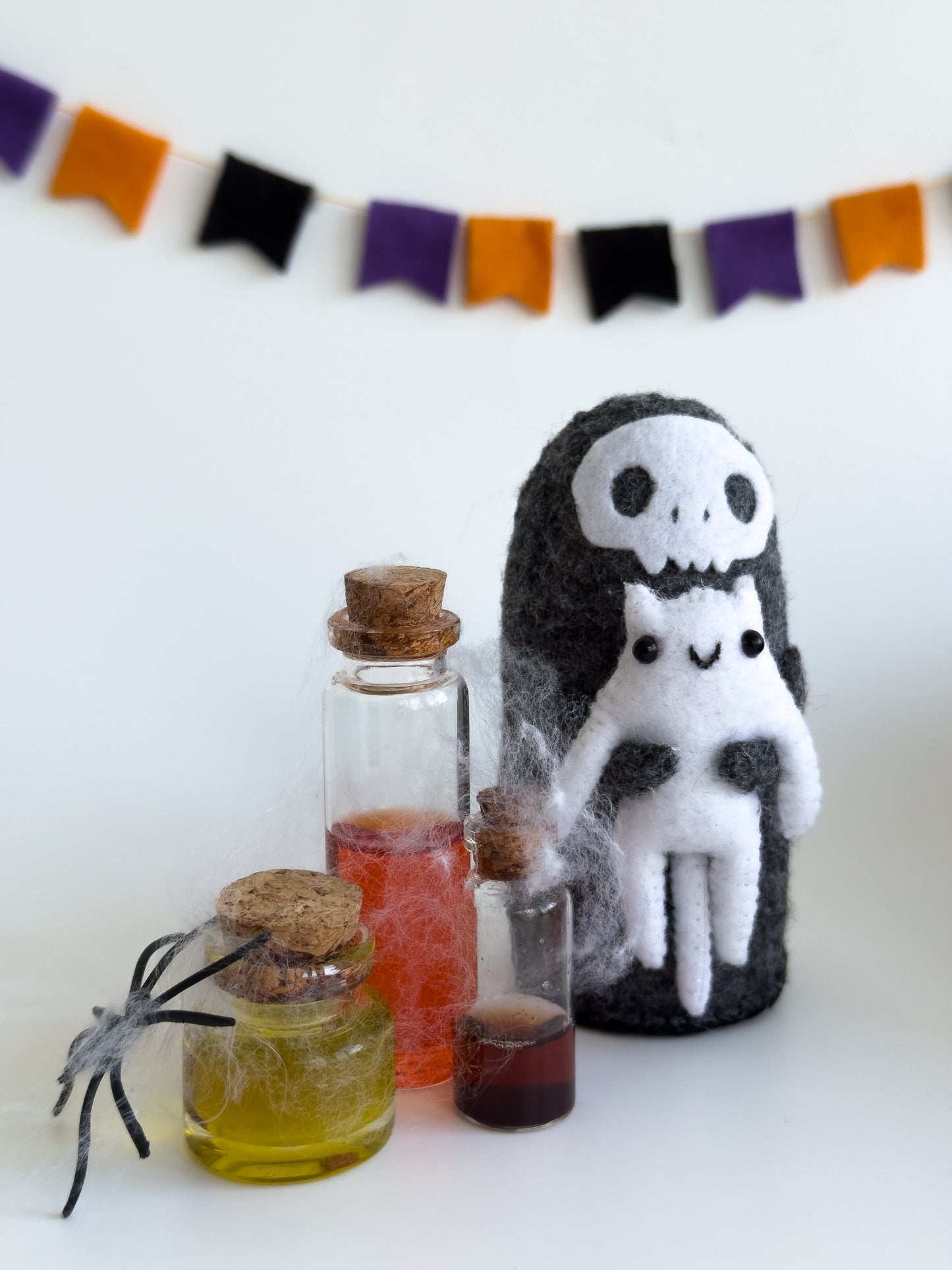 Gothic felt reaper doll next to spellbook and cobweb props – spooky setting