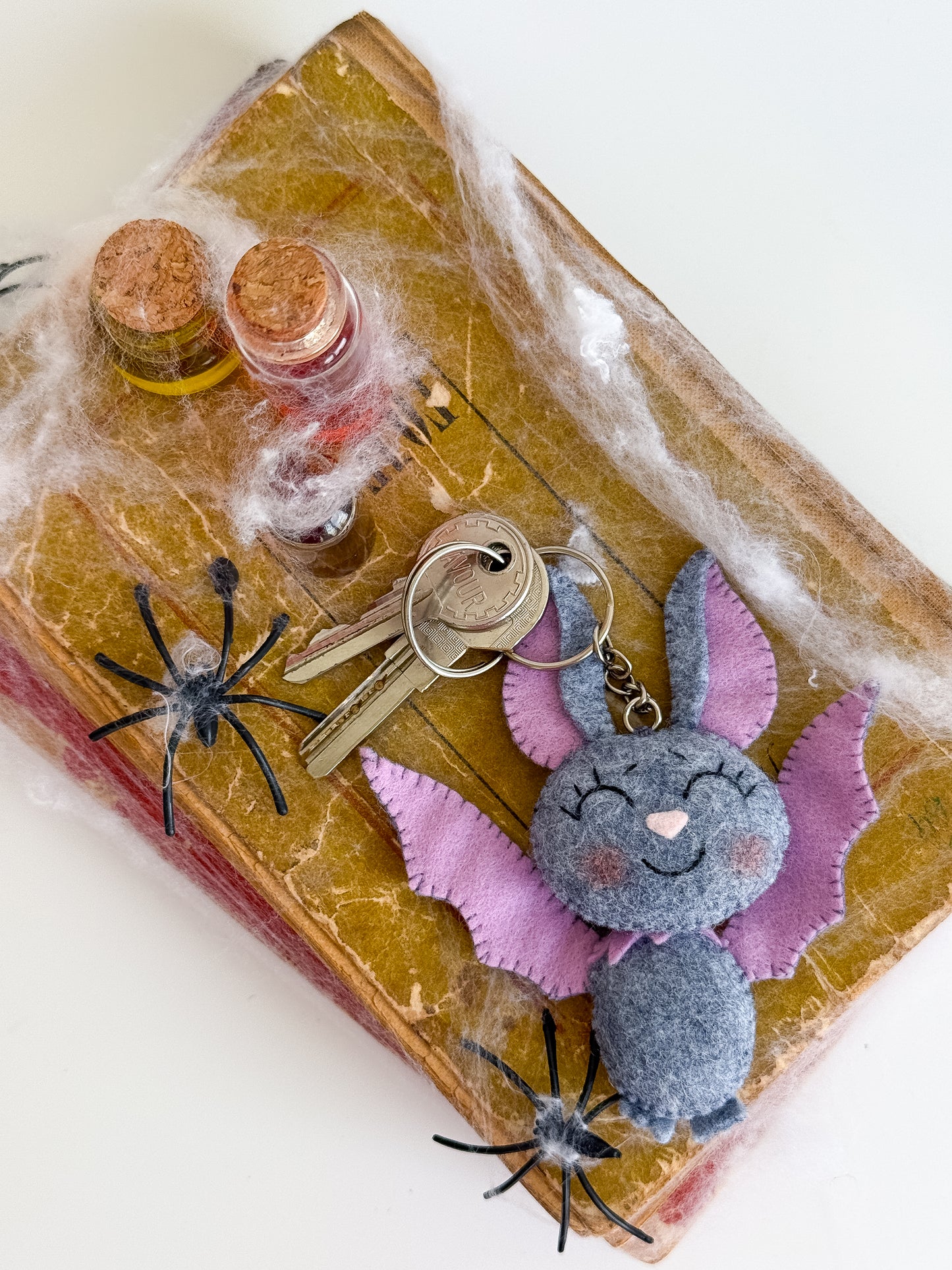 Gothic bat keychain made from grey and purple felt, hanging from a metal chain with keys