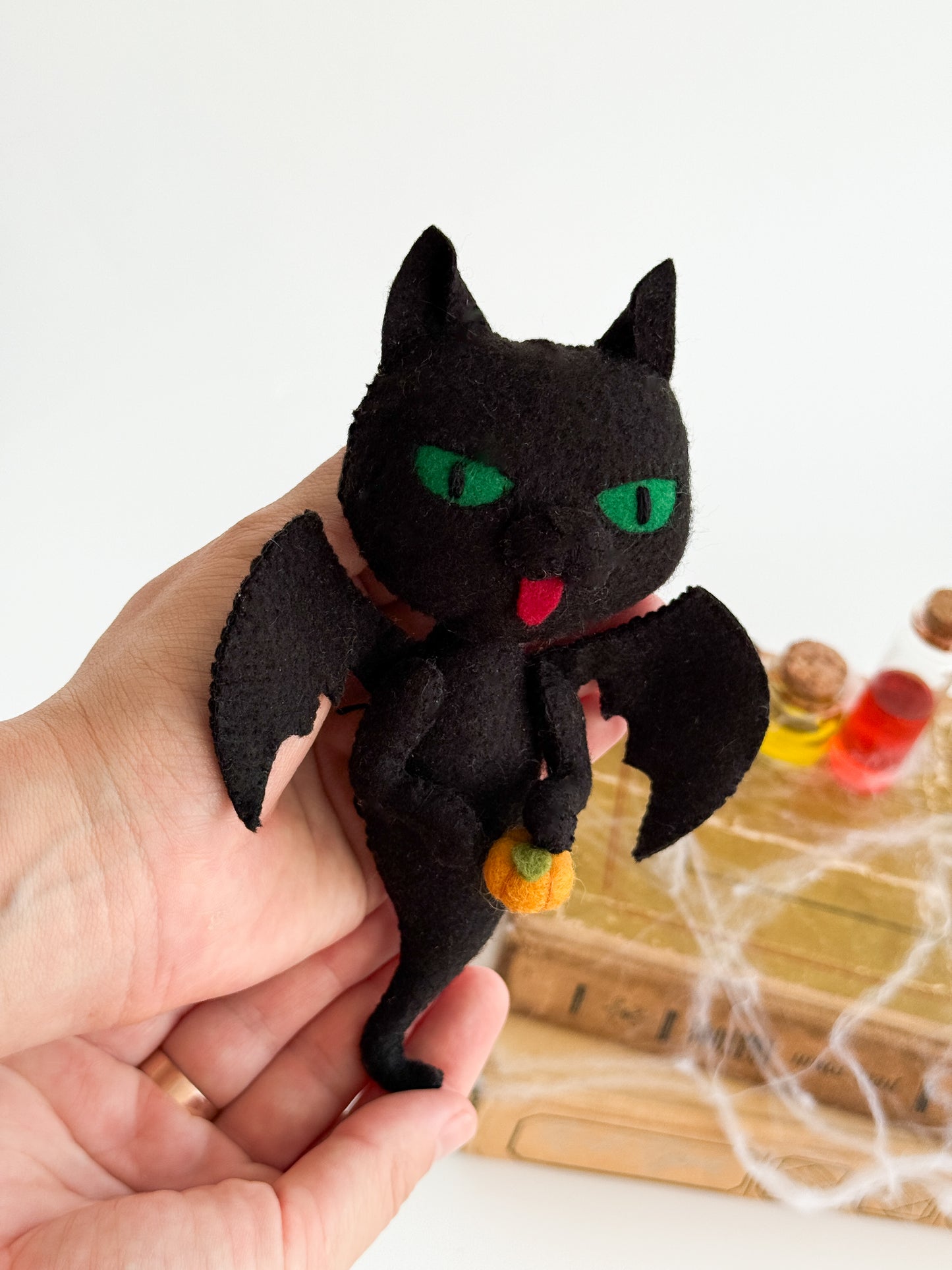 Soft felt Halloween ornament shaped like a black cat ghost holding a pumpkin, handmade seasonal decoration.