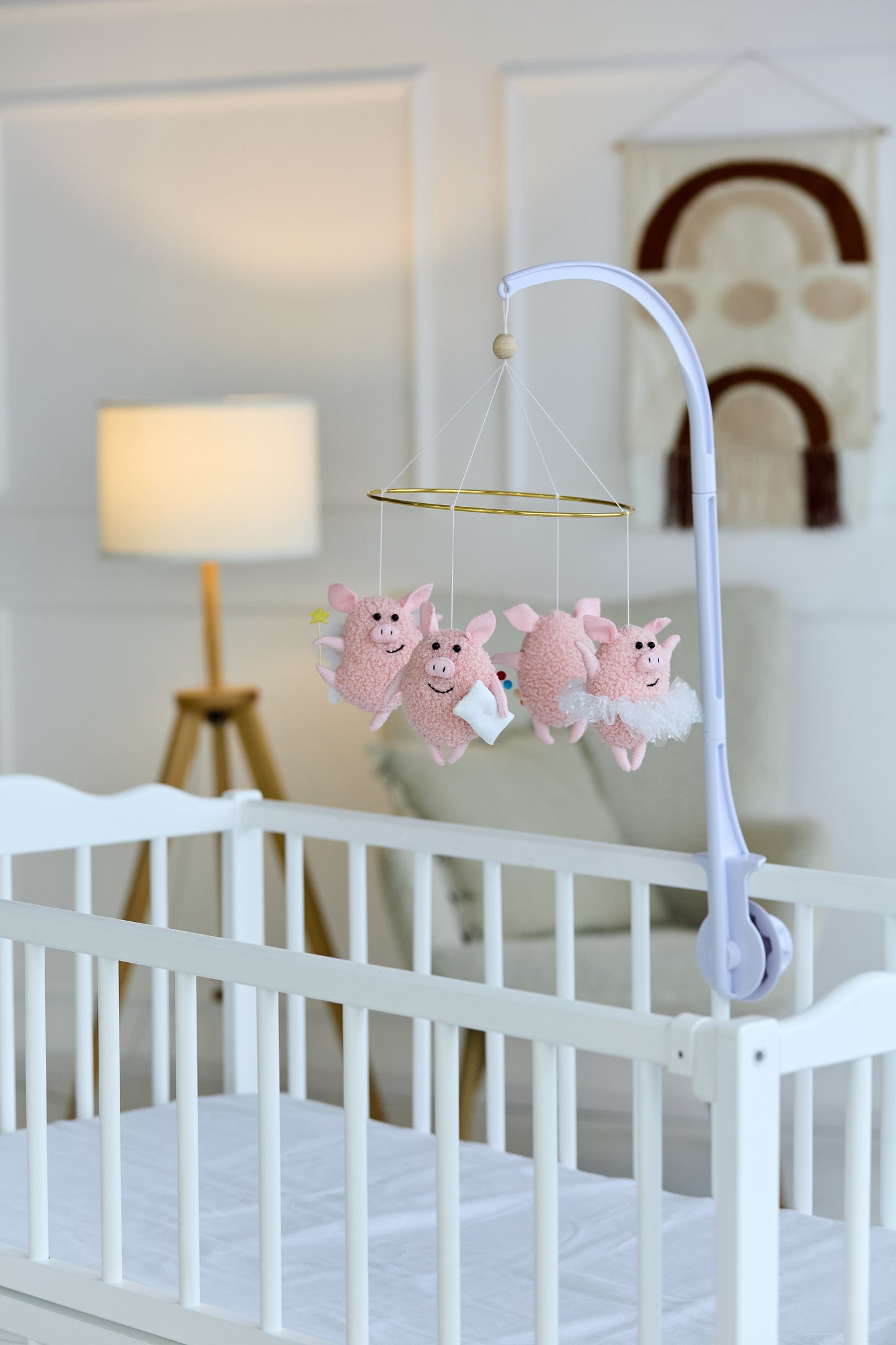 Felt pig baby mobile hanging over a crib in soft pink tones