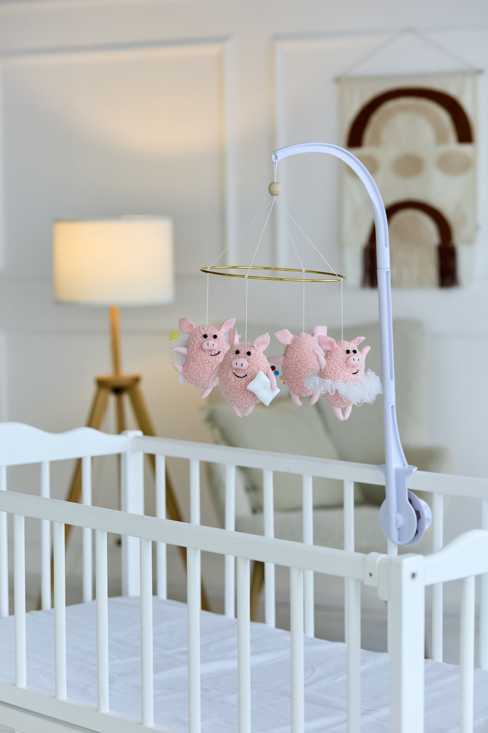 Felt pig baby mobile hanging over a crib in soft pink tones