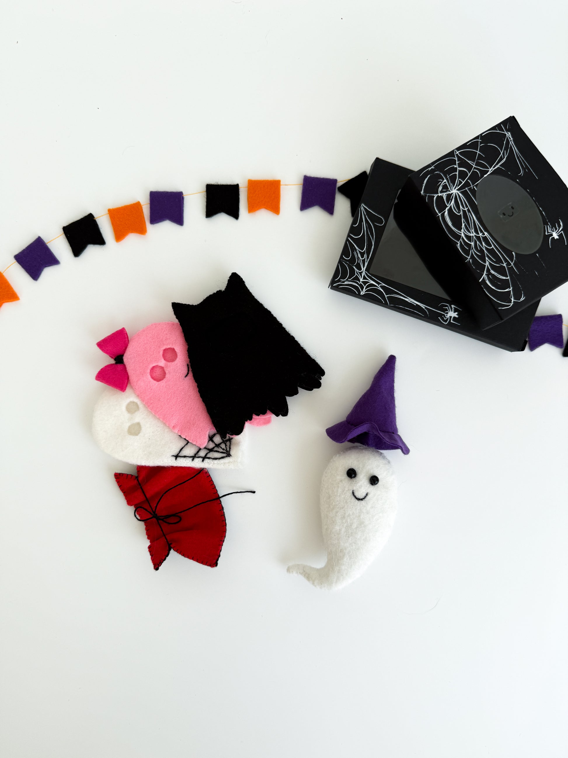 Felt ghost toy with purple witch hat and Halloween costumes next to black spiderweb gift boxes
